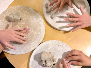 Bild på händer och lera vid ett bord. 